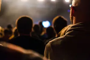 Audience silhouettes watching a performance under bright stage lights, creating an intimate and electrifying atmosphere.