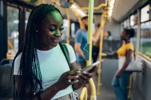 Smiling woman using a smartphone on a bus, surrounded by other passengers, showcasing urban commuting life.