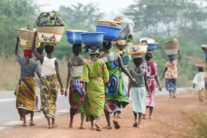 Women walking along a rural road, carrying colorful baskets on their heads, showcasing traditional attire and community life.