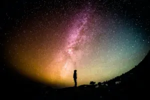 A silhouette of a person gazes at a vibrant night sky filled with stars and the Milky Way galaxy.