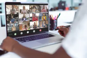 Person participating in a virtual meeting on a laptop, showing multiple video conference attendees on screen.