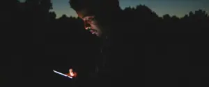 Person using a smartphone in the dark, with a twilight backdrop creating a serene evening atmosphere.