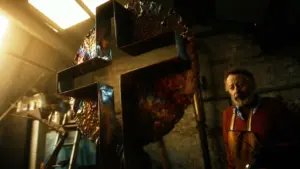 A person standing next to a large artistic cross in a dimly lit workshop, highlighting craftsmanship and creativity.