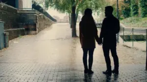 Silhouetted couple holding hands under a tree-lined walkway on a rainy day, creating a romantic atmosphere.