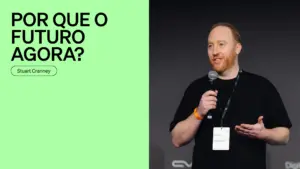 Person speaking at a conference, with a vibrant green background and text highlighting the topic "Por Que o Futuro Agora?"