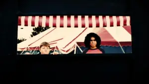 Two kids standing in front of a colorful striped tent, capturing a playful carnival atmosphere.