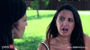 Two women engaged in a serious conversation outdoors, surrounded by greenery, expressing strong emotions.