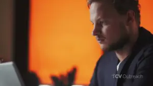 Man focused on a laptop with an orange background, depicting concentration and tech engagement in a modern setting.