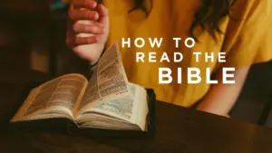 Open Bible resting on a table with a person's hand holding a pen, focused on "How to Read the Bible" text overlay.