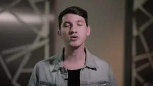 Young man in a denim jacket speaking in a softly lit environment, focused expression, engaging with the audience.