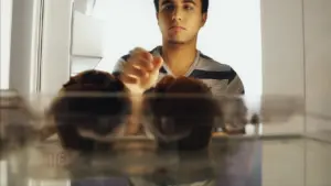 Young man reaching for cupcakes inside a refrigerator, showcasing a moment of indulgence and desire for a sweet treat.