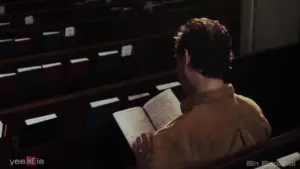 Man reading a book alone in a church pew, with empty seats and soft lighting highlighting the serene atmosphere.