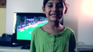 Smiling child in green top in front of a TV displaying a soccer game, radiating joy and excitement.