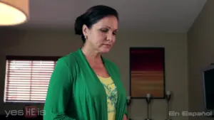 Woman in a green cardigan stands thoughtfully in a cozy, softly lit living room with decorative elements.