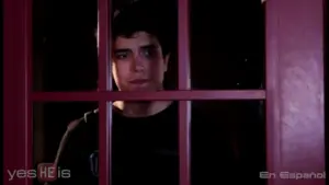 Young man with a concerned expression looking through a red-framed window, portraying a sense of vulnerability.