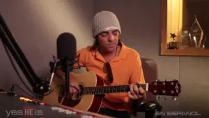 Musician in a beanie playing acoustic guitar in a recording studio, focused on creating music.