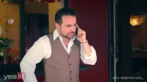 Man in a vest speaking on the phone outside a vibrant restaurant, showcasing a stylish urban atmosphere.