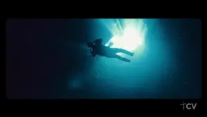 A silhouette of a diver floating underwater, illuminated by bright blue light from above, creating an ethereal atmosphere.