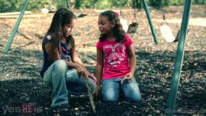 Two young girls playing on a playground, exploring the ground and enjoying their time outdoors.