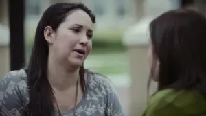 Two women engaged in a serious conversation outdoors, with soft expressions and a blurred park background.