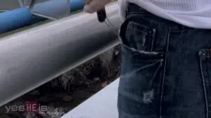 Person wearing distressed jeans with knife partially visible, standing near a metallic structure outdoors.