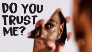 A person looking into a broken mirror with the text "Do you trust me?" in a bold font, symbolizing self-reflection.