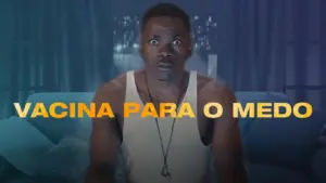 Man sitting on a couch with a shocked expression, the text "VACINA PARA O MEDO" prominently displayed above him.