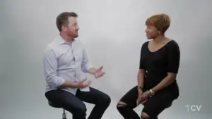 Two professionals engaged in a conversation, seated against a neutral background, showcasing a dynamic discussion.