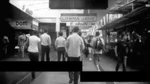 Black and white street scene of pedestrians walking by shops, highlighting urban life and retail activity.