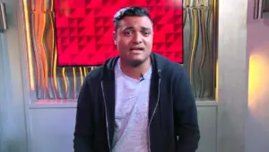 Young man in a black hoodie stands in front of a vibrant red geometric backdrop with bright lighting.