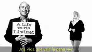 Man holding a sign that reads "A Life Worth Living" alongside a woman speaking, set against a white background.