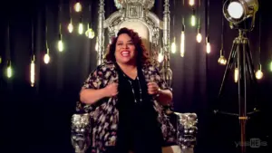 Smiling woman in a stylish outfit seated on a silver throne, with warm lights creating a vibrant atmosphere.