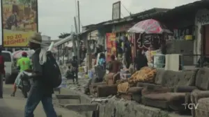 Busy street market scene with vendors, colorful umbrellas, and pedestrians navigating through a lively urban landscape.