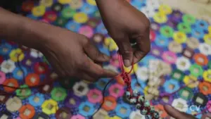 Hands crafting colorful jewelry against a vibrant hexagonal-patterned background, highlighting artisanal skills and creativity.