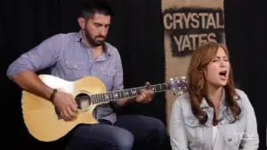 Musicians performing live, featuring a man with a guitar and a woman singing, against a backdrop with "Crystal Yates."