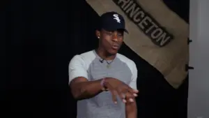 Young man gesturing, wearing a cap and casual shirt, with a Princeton banner in the background.