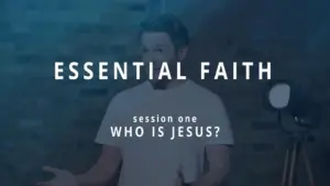 Person presenting "Essential Faith" session on "Who is Jesus?" with spotlight and brick background. Engaging faith discussion.