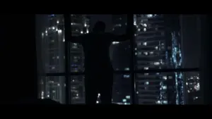 Silhouette of a person gazing out of a window at a vibrant city skyline illuminated at night.