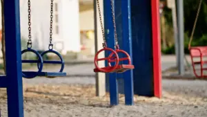 Colorful playground swings in a sandy area, featuring blue and red seats suspended from sturdy frames.