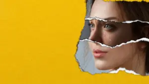 Woman's face partially revealed through torn yellow paper, highlighting expressive eyes and emotional depth.