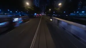 Nighttime city street with blurred lights from passing cars, illuminated buildings, and a sense of speed and motion.