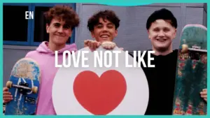 Three smiling friends holding a large heart symbol and skateboards, promoting a message of love.