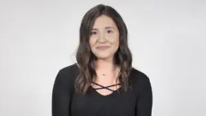 Smiling woman with long hair in a black top against a plain background, conveying warmth and approachability.