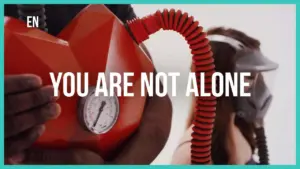 Red inflatable device and person wearing a mask with the message "You Are Not Alone" prominently displayed in bold text.