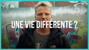 Man in a black jacket stands before a colorful graffiti wall, asking, "A different life?" in bold white text.