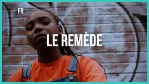 Young person with a serious expression in an orange shirt stands against a brick wall featuring graffiti art, promoting "Le Remède."