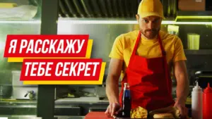 Man in a yellow shirt and cap, wearing an apron, prepares food in a vibrant restaurant kitchen setting.