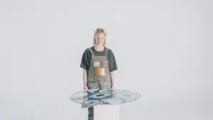 Person standing beside a modern glass table, showcasing artistic designs against a minimalist light background.