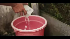 Person pouring water from a container into a pink bucket, highlighting the process of filling it up.