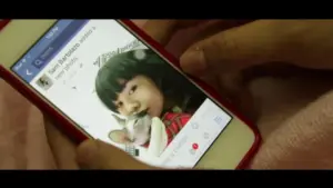 Person holding a smartphone displaying a photo of a girl with a cat, social media interface visible on screen.